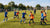 Een groep spelers traint op het veld, geconcentreerd op passing en tactiek met een coach aan de zijlijn.