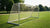 Een aluminium voetbaldoel staat buiten, bevroren gras eromheen, met een houten opslagplaats op de achtergrond.