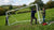 Een voetbaldoel staat op een hellend veld, met een bal en spelers op de achtergrond die zich voorbereiden op een training.