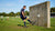 Speler test rebounder met bal, terwijl een trainer aanwijzingen geeft tegen een muur op een veld.