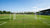 Vaste voetbaldoelen op een oefenveld met spelers die trainen en de bal passen. Achtergrond met tribunes en bomen.