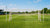 Groot voetbaldoel met netten op een grasveld, omringd door spelers in actie tijdens een training.