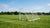 Een verplaatsbaar voetbaldoel op een grasveld met spelers die oefenen in de achtergrond.