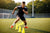 Voetballer tijdens een agility training op een voetbalveld. Op de achtergrond een voetbaldoel & tribune.
